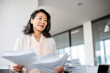 Mature Asian organizer setting up an employee wellness program, distributing flyers in a bright office