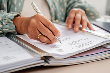 Elderly Hispanic woman editing a company handbook, cross-checking legal compliance and internal notes while referencing past versions