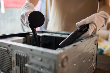 A man cleans a computer case with a vacuum in a bright room, stressing workspace tidiness