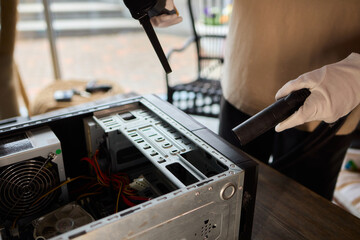 A man cleans a computer case with a vacuum in a bright room, stressing workspace tidiness