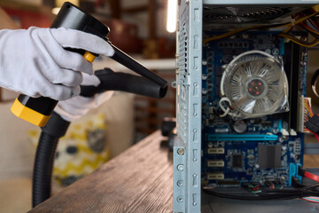A man cleans a computer case with a vacuum in a bright room, stressing workspace tidiness