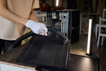 A man cleans a computer case with a vacuum in a bright room, stressing workspace tidiness