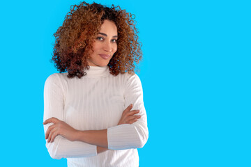 Confident woman with curly hair poses with crossed arms against  bright blue background in studio...