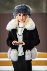 Portrait of a young beautiful blonde model-looking girl in winter clothes and a fur hat in winter.