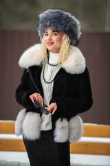 Portrait of a young beautiful blonde model-looking girl in winter clothes and a fur hat in winter.