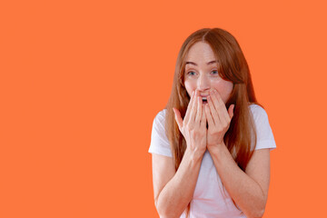 Excited woman expressing surprise and joy against a vibrant orange background during an afternoon...