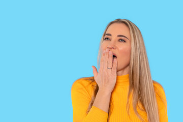 Woman in yellow sweater yawning against bright blue background during indoor activity in a relaxed...