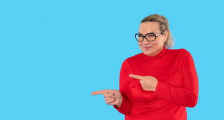 Woman in red shirt smiling and pointing at camera against a bright blue background during a relaxed...