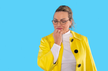 Confident woman in a bright yellow coat contemplating with a thoughtful expression against a...