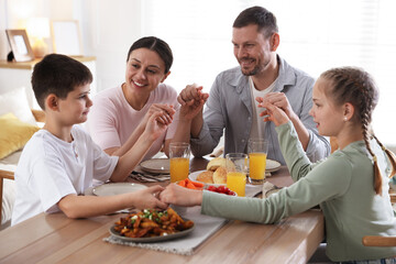 Family praying together before dinner at table indoors
