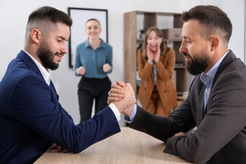 Businessmen arm wrestling at wooden table in office, selective focus