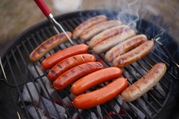 Delicious grilled sausages on a barbecue with smoke rising during a summer cookout and outdoor cooking experience, culinary photography.
