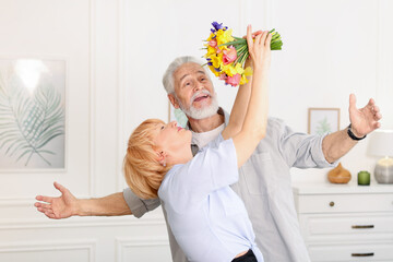 Lovely senior couple with bouquet of flowers at home