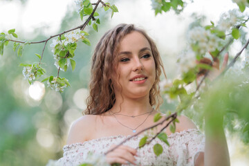 Beautiful Girl with long hair in a white dress poses near white blossoming apple trees