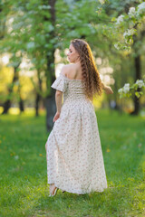 Beautiful Girl with long hair in a white dress poses near white blossoming apple trees