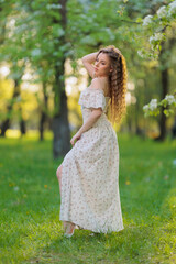 Beautiful Girl with long hair in a white dress poses near white blossoming apple trees