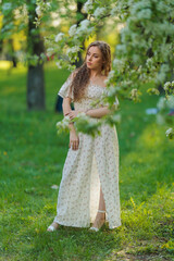 Beautiful Girl with long hair in a white dress poses near white blossoming apple trees