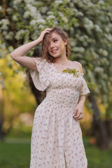 Fototapeta premium Beautiful Girl with long hair in a white dress poses near white blossoming apple trees