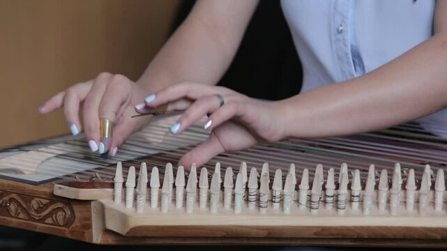 Close-up of a musician's hands playing a traditional string instrument, likely a kanoon. The intricate captures the essence of classic Middle Eastern music during a cultural performance.