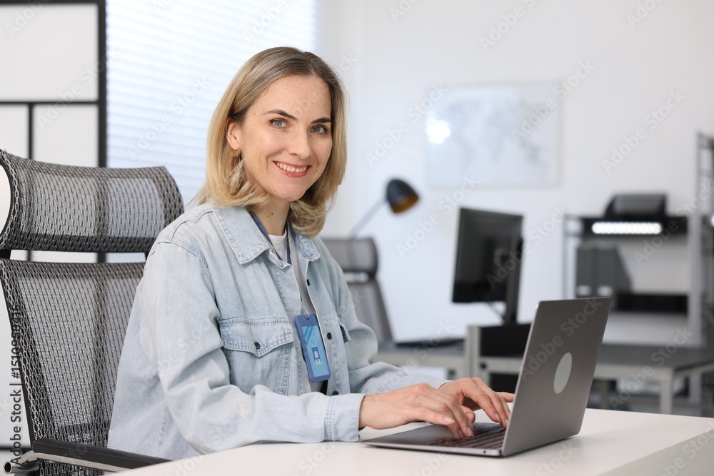 Poster smiling engineer working with laptop at table in office