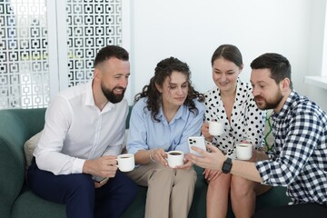 Man showing colleagues something on his phone during coffee break in office