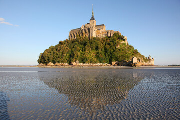 view of famous Le Mont Saint-Michel tidal island with clear water and beautiful reflections on a sunny day, Normandy, northern France