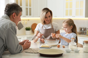 Happy parents and their daughter making dough at white marble table in kitchen