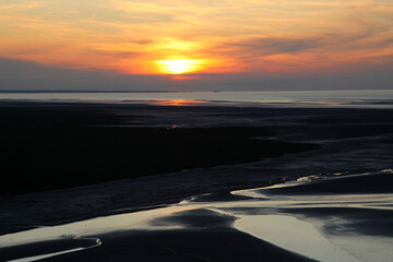 Sunset above the low tide mudflats and channels of the seaward of Mont St Michel in Normandy, France