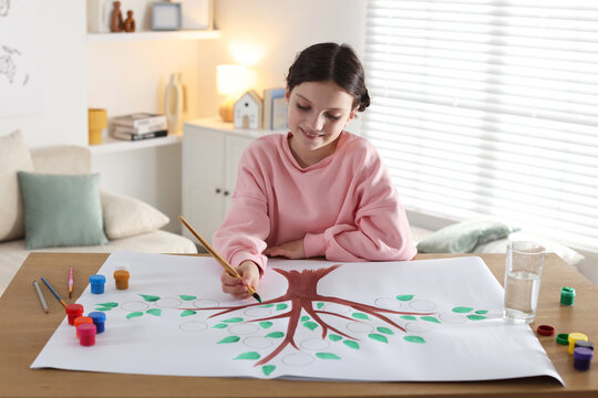 Girl drawing her family tree with paints at wooden table indoors