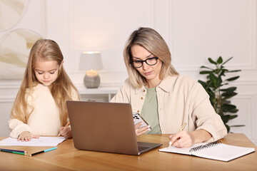 Single mother working and her daughter drawing at wooden table indoors