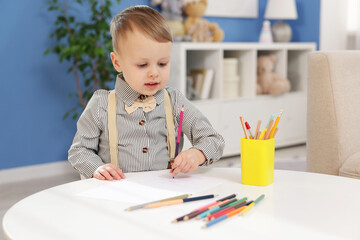 Little boy with colorful pencils at table indoors