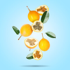 Delicious ripe passion fruits with green leaves falling on light blue background