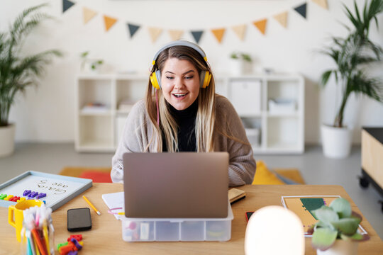 A teacher is leading a virtual class from her home. She's using her laptop and headset to connect with students and provide instruction.