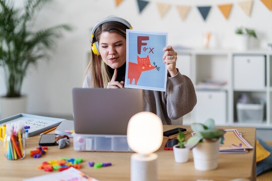 A teacher is leading a virtual class, holding up a picture of a fox to teach the letter F. She's using online tools to connect with students remotely.