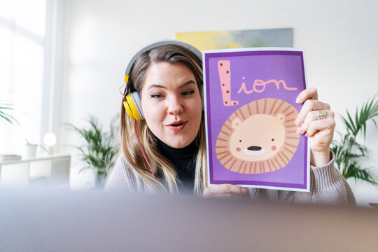 A teacher is leading a virtual lesson, showing a picture of a lion to help kids learn the alphabet. She's using technology to connect and educate.