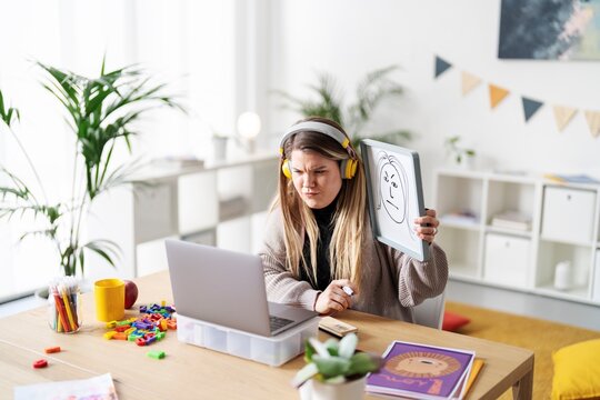 A teacher is leading a virtual class, using a whiteboard to draw a face. She looks concerned, perhaps because she's trying to engage her students remotely.