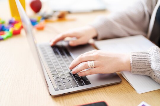 A person is working on a laptop at a wooden desk. They are likely working from home, as there are children's toys nearby.