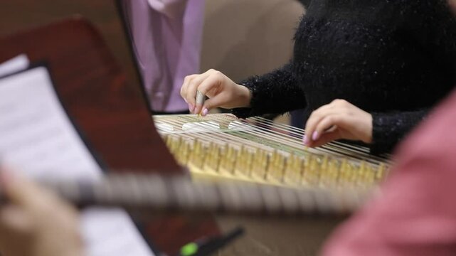 Close-up of a musician's hands playing a traditional string instrument, likely a kanoon. The intricate captures the essence of classic Middle Eastern music during a cultural performance.