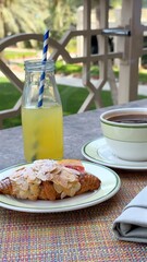 Freshly baked almond croissant dusted with powdered sugar, accompanied by fresh fruit, orange juice, and coffee on sunlit garden terrace