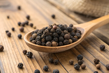 Black peppercorns in a wooden spoon arranged on a rustic wooden surface culinary ingredient for cooking and seasoning