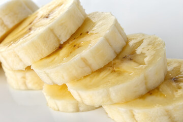 A detailed close-up shot of freshly sliced ripe banana pieces arranged on a clean white background.