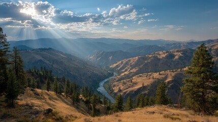   The sun illuminates the valley through the cloudy sky, with a river in the foreground and majestic mountains in the background