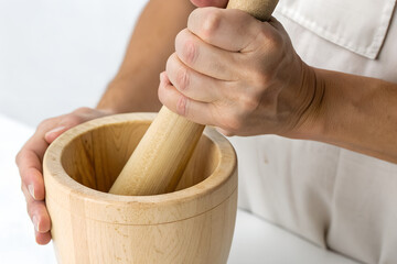 Hands grinding with a wooden mortar and pestle.