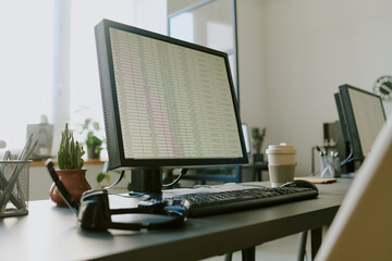 Office workspace featuring monitor displaying spreadsheet with coffee cup, keyboard, and headphones adding productivity tools to clean, modern desk setup