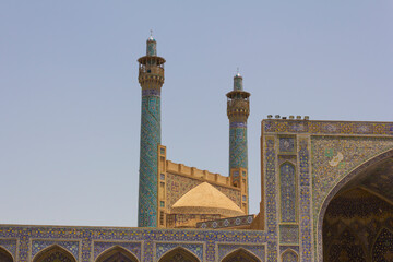 The stunning architecture of the Shah Mosque in Isfahan, Iran, featuring intricate tile work and towering minarets against a clear sky.