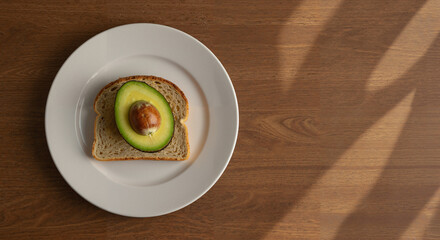 Avocado on whole grain toast served on a white plate against wood  