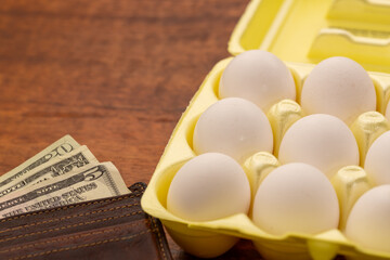 Wallet with money next to a white chciken eggs in a yellow carton concept high egg prices copy space