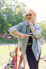 Portrait young adult pretty woman with red vintage retro bike and pin-up casual outfit green city park bright sunny summer day. Happy beautiful female person cycling outdoors. Healthy lifestyle