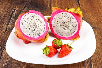 Pitahaya fruit cut into two parts on a white plate with strawberries.