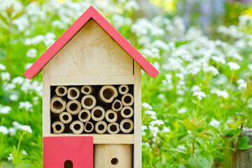 An insect hotel or bee hotel in a summer garden with flowers. An insect hotel is a manmade structure created to provide shelter for insects in a variety of shapes and sizes and materials.	